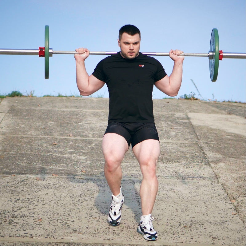 Man performing a barbell squat outdoors on a concrete surface with a clear blue sky. (Torokhtiy Weightlifting)