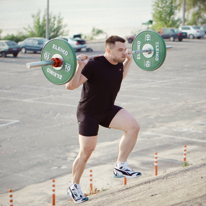 Man lifting a barbell with green plates in an outdoor setting  (Torokhtiy Weightlifting)