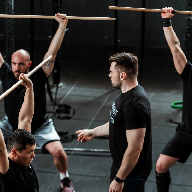 Group of men exercising with wooden bars in a gym setting (TOROKHTIY WEIGHTLIFTING)