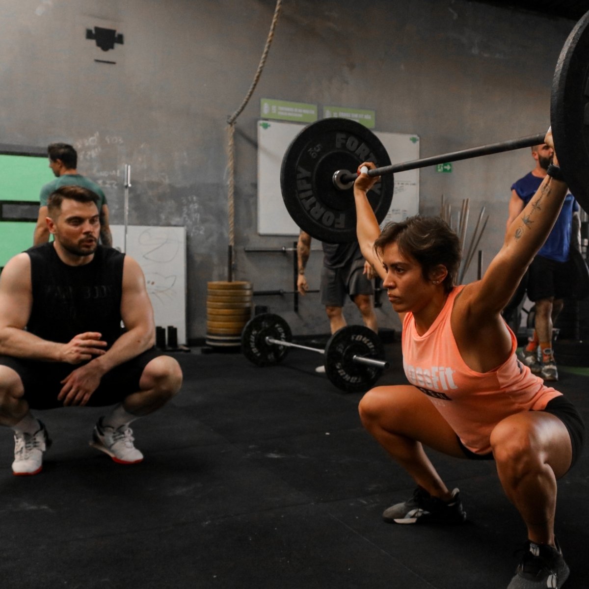 Woman lifting weights with a coach observing in a gym setting (Torokhtiy Weightlifting)