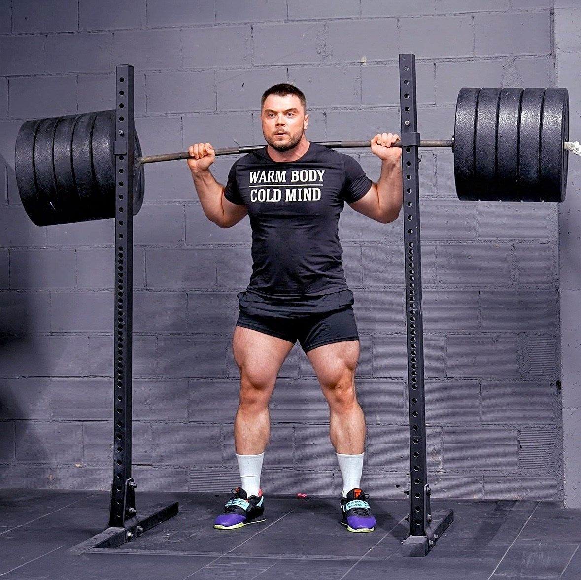 Man lifting a barbell in a gym setting with a gray brick wall background (Torokhtiy Weightlifting)